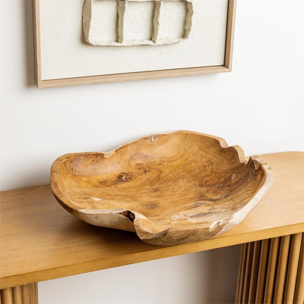 Organic-shaped hand-carved teak wood decorative bowl on a modern wooden console table with minimalist wall art.