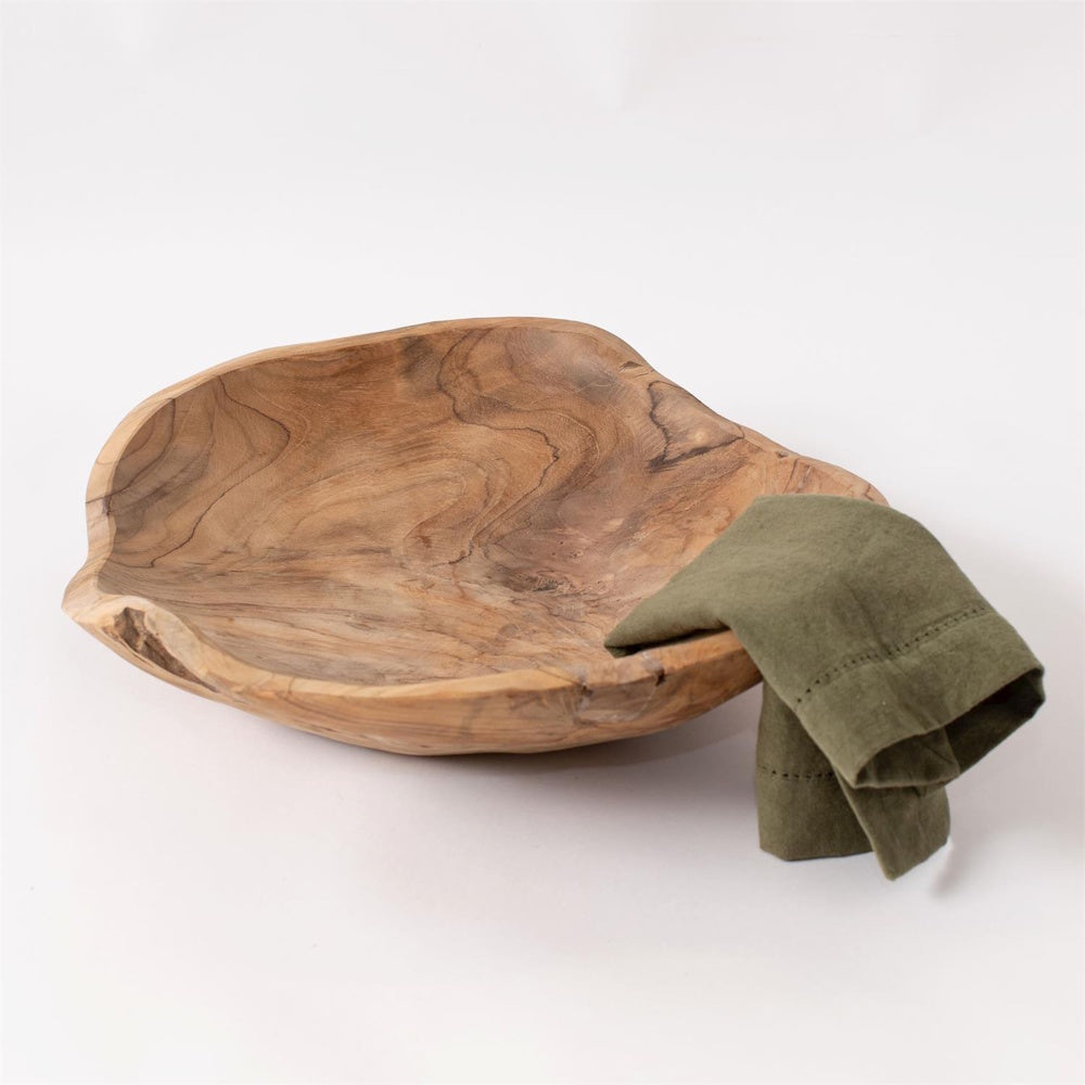 Hand-carved organic teak wood bowl with a natural grain finish and olive green linen napkin on a white background.