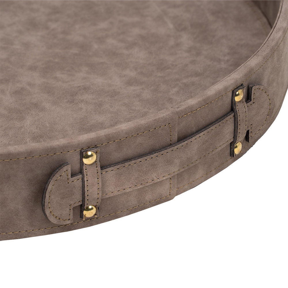 Close-up of a round, taupe faux leather tray featuring a stitched side strap with decorative gold metal rivets.