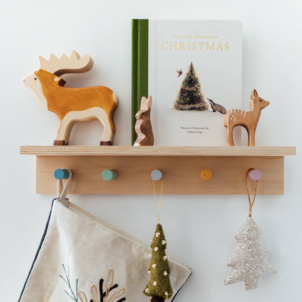 Wooden shelf with "Our Little Adventure at Christmas" book, wooden animal toys, and hanging holiday stockings.