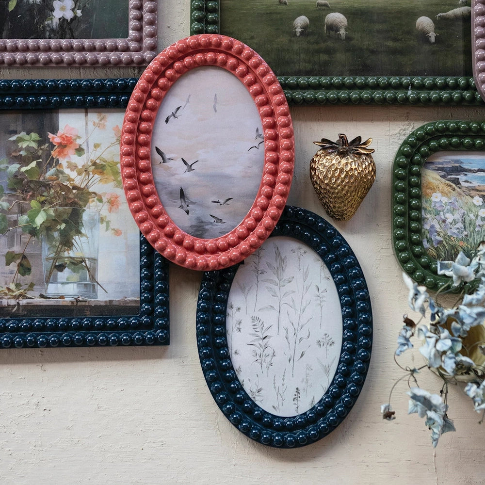 Pink, blue, and green bobbin-style oval frames with art on a wall, featuring a gold strawberry wall hook.