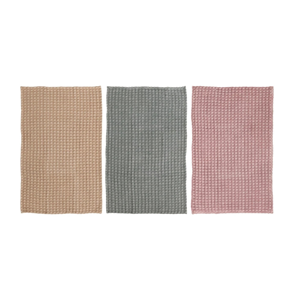 Three stonewashed cotton waffle weave tea towels in tan, sage green, and dusty rose against a white background.