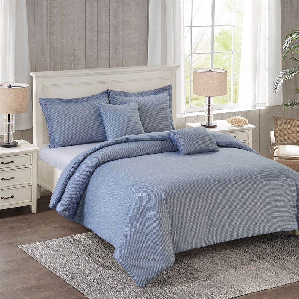 A bedroom set featuring a white wooden bed made up with textured blue bedding, pillows, and a gray area rug.