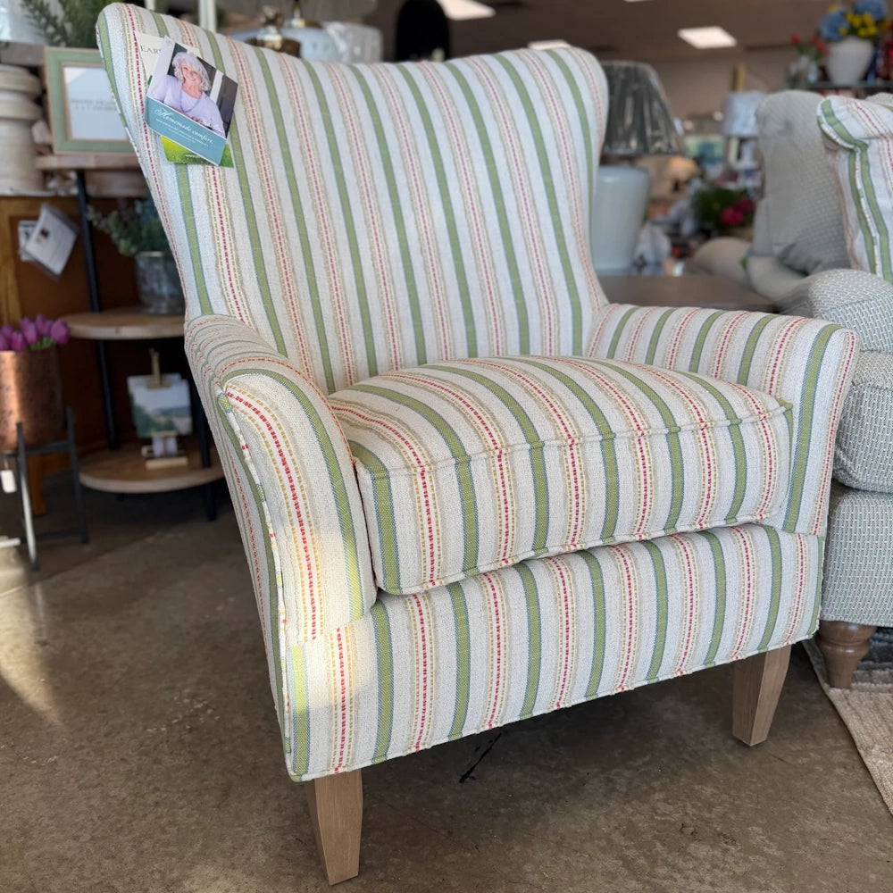 A upholstered wingback armchair with vertical green and beige striped fabric and light wood legs.