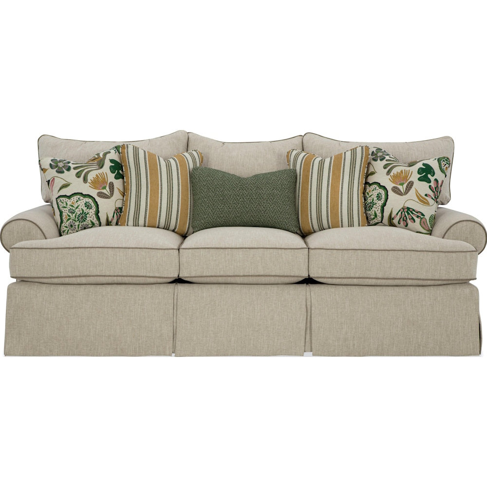 Front view of a beige skirted three-cushion sofa featuring striped and floral pillows on a white background.