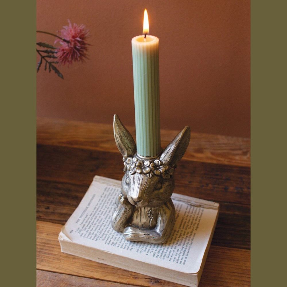 Gold rabbit taper candle holder with flower crown on a vintage book, holding a lit green ribbed candle for home decor.