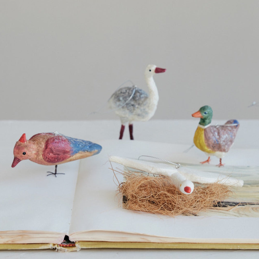 Paper-mache vintage-style bird and goose ornaments displayed together on an open book.
