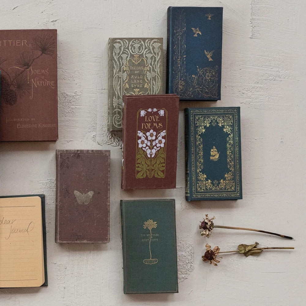 Flat lay of vintage hardcover books with floral gold-leaf designs, dried flowers, and a handwritten journal.