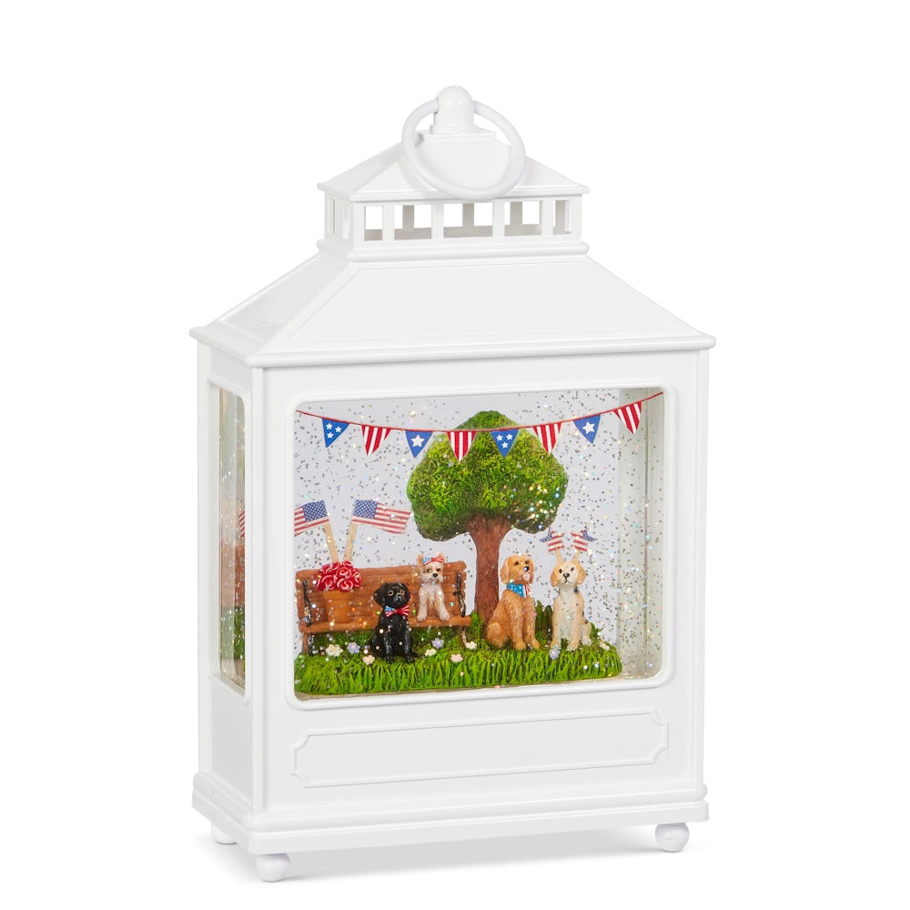 A decorative white lantern features a festive scene inside. Dogs sit on grass near a tree, surrounded by American flags and bunting, amid glittering snow.