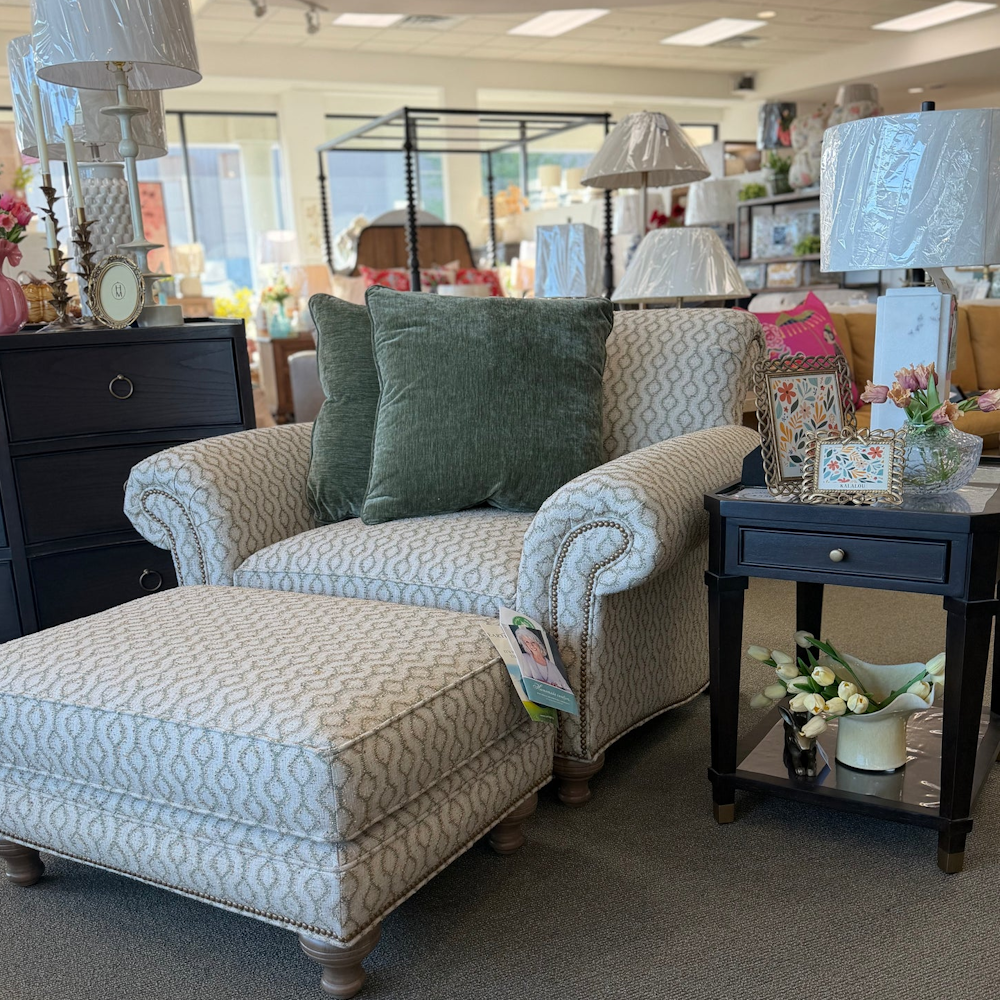 Patterned upholstered armchair with matching ottoman, green pillows, nailhead trim, and side table.