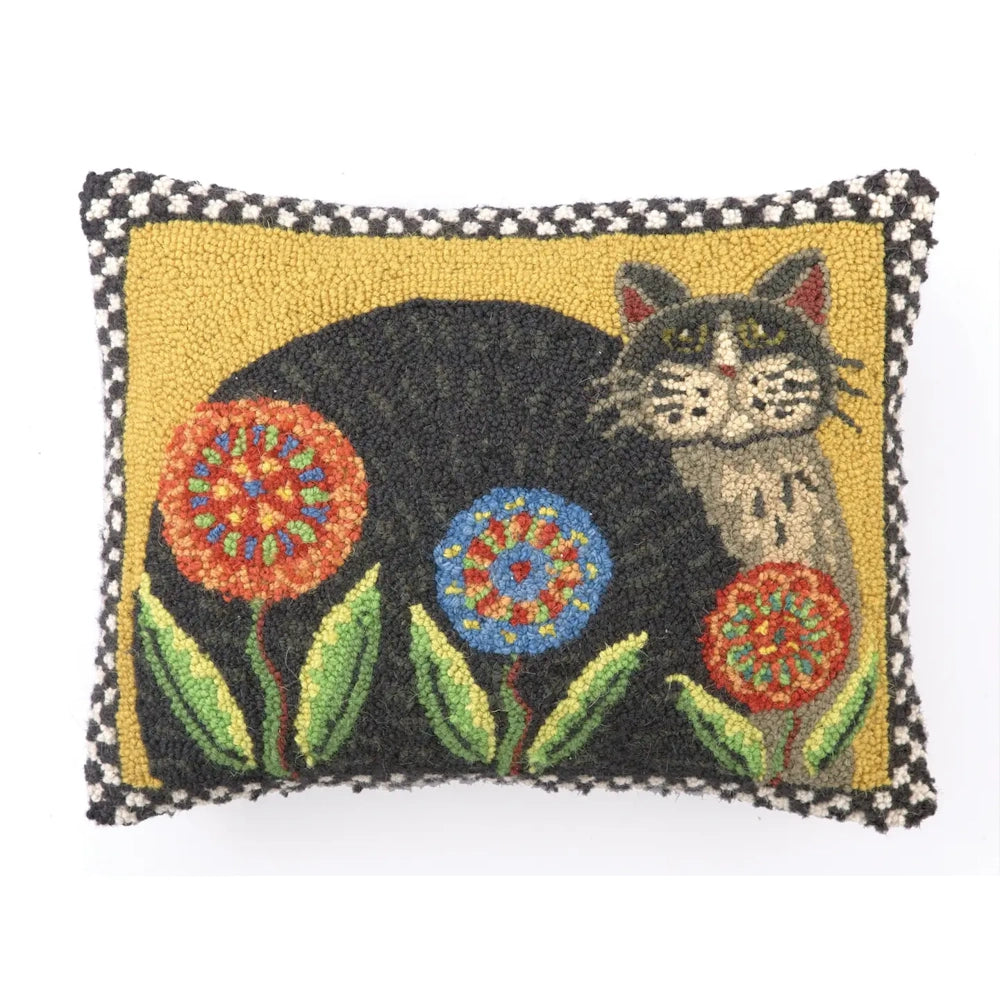 A hook rug pillow featuring a black and grey cat sitting among colorful flowers on a yellow background.