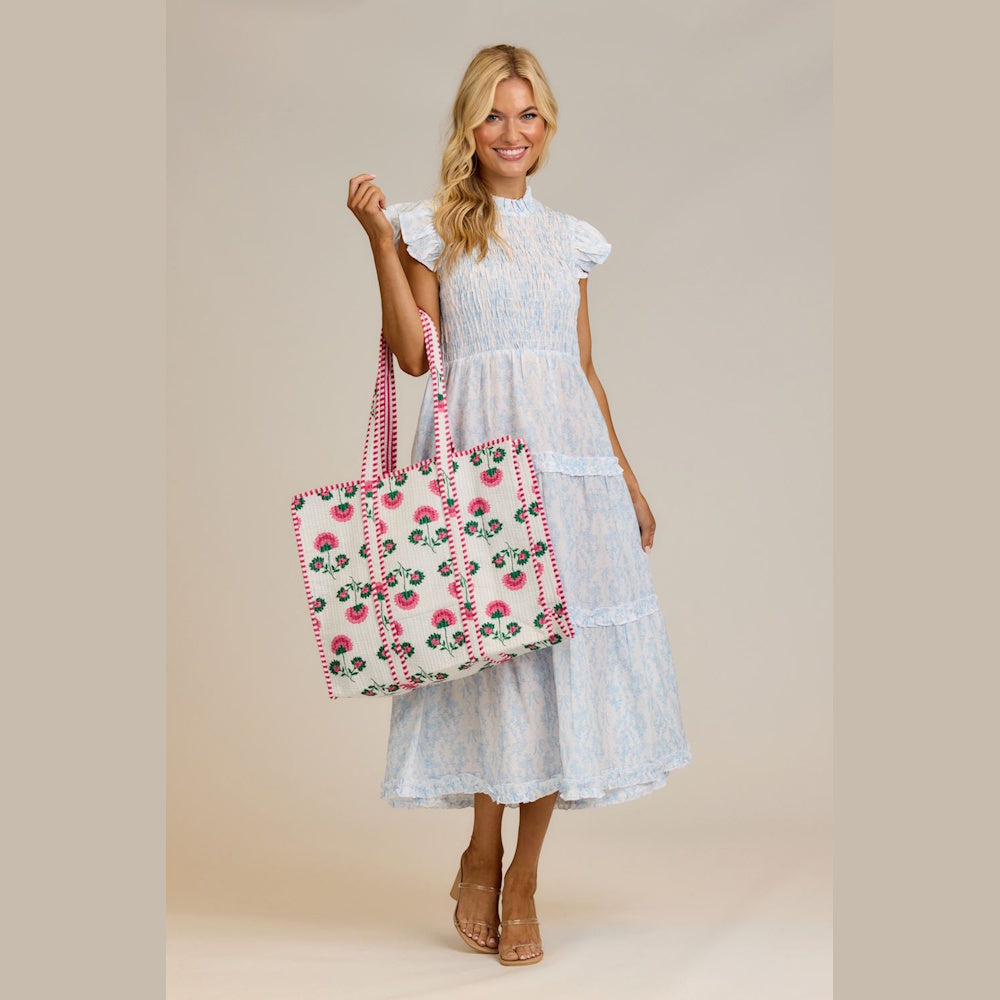 Woman in light blue tiered dress holding a pink floral block print quilted tote bag.