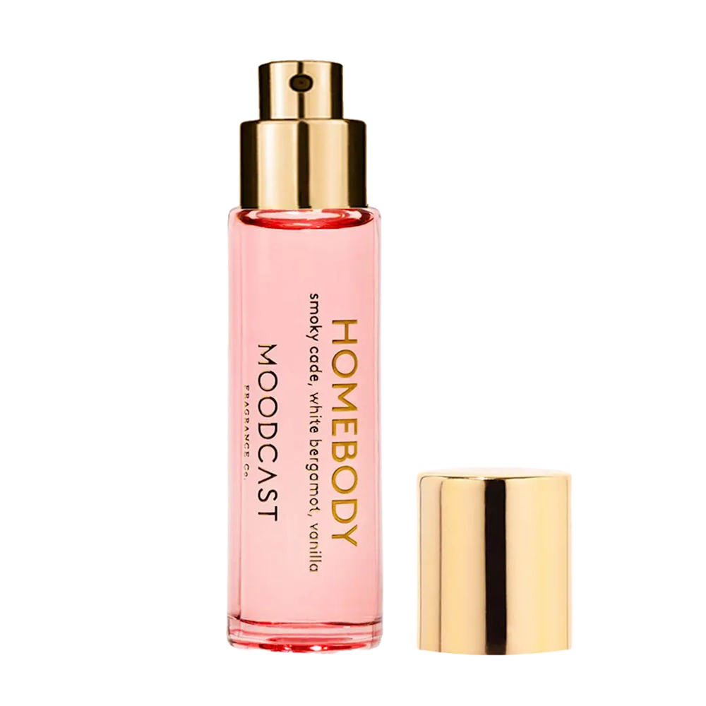 Moodcast Homebody perfume mist bottle in clear glass with pink liquid, gold pump sprayer, and gold cap beside it.