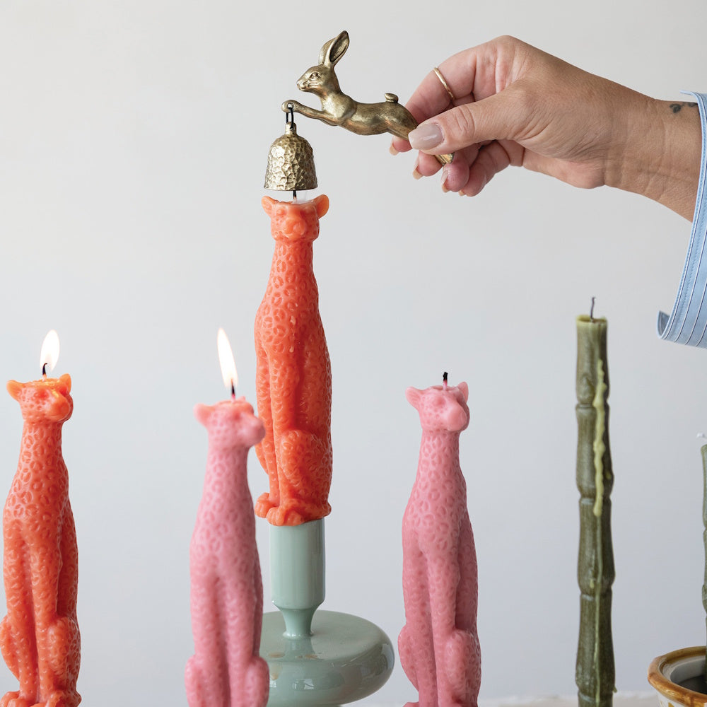 Pewter rabbit candle snuffer extinguishing an orange cheetah shaped candle.
