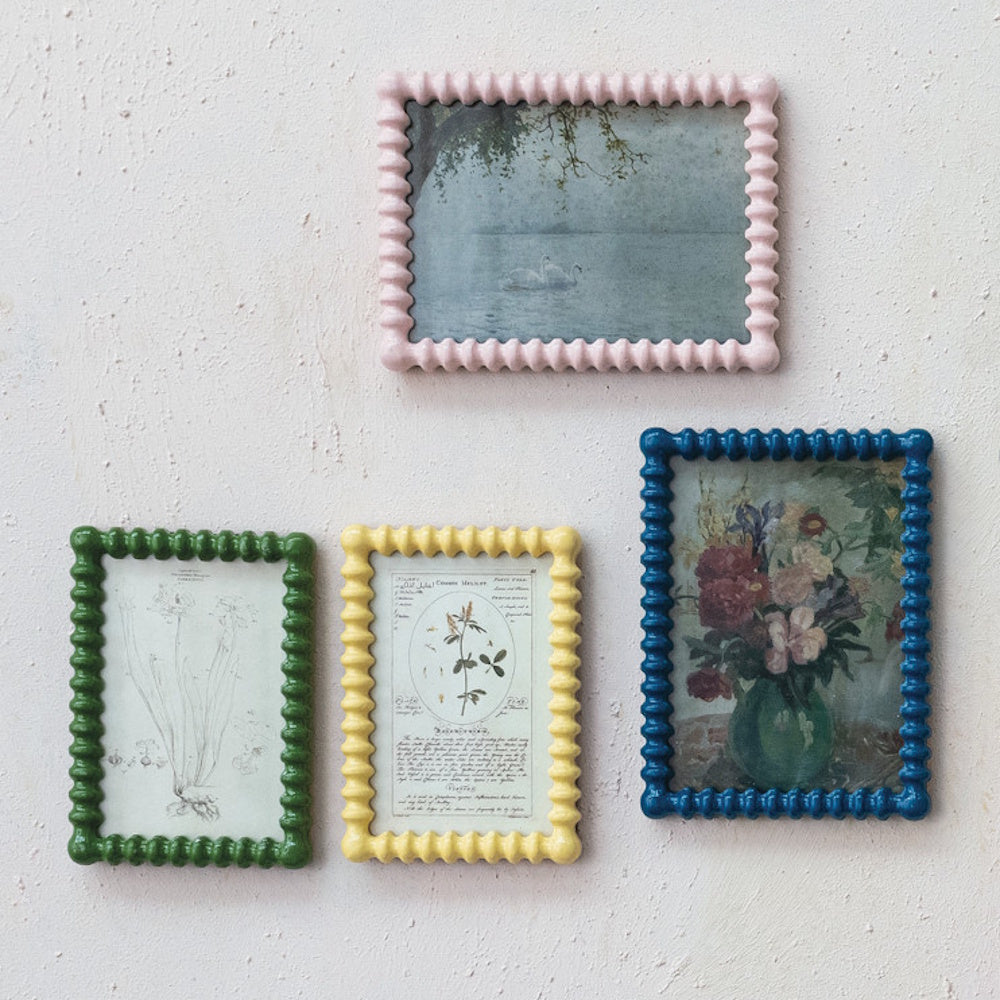 Collection of textured picture frames in pink, green, yellow, and blue displayed hanging on a white wall with vintage art prints.