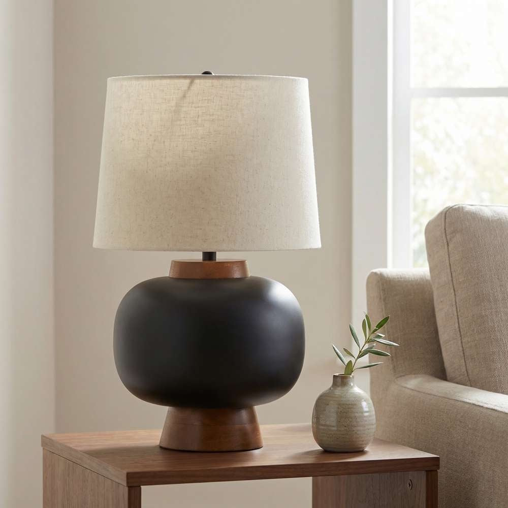 Modern matte black table lamp with wood accents and linen shade on a wooden nightstand.