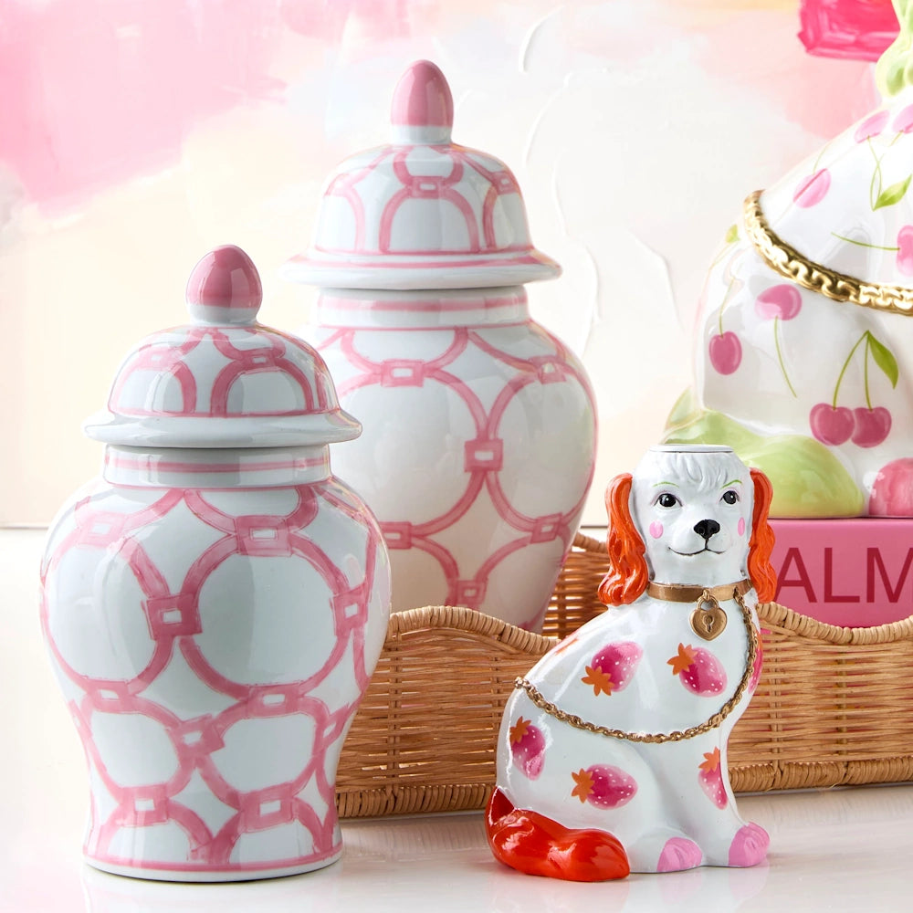 Two pink and white geometric ginger jars stand behind a ceramic spaniel figurine decorated with strawberries on a tray.