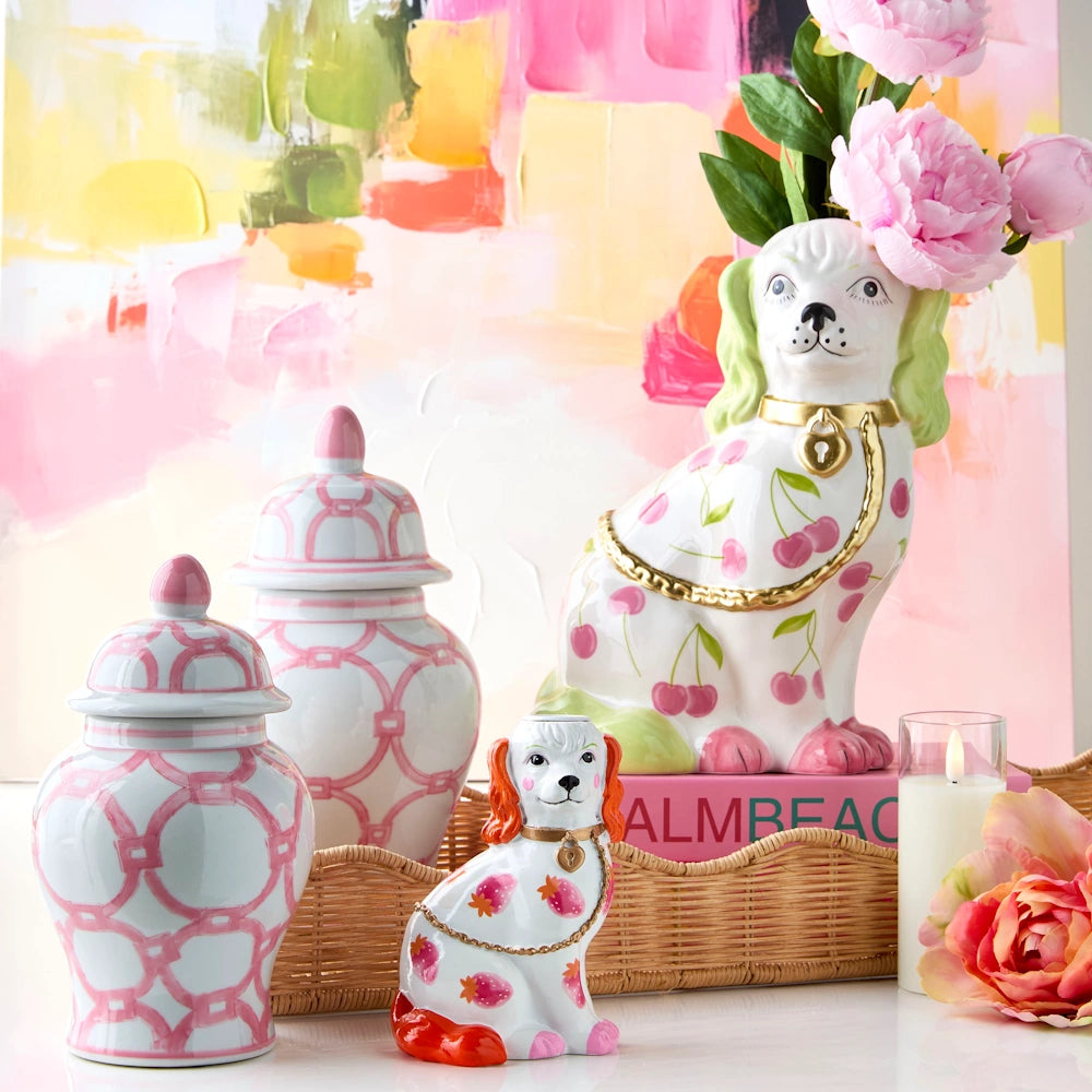 Two ceramic pink-patterned ginger jars and two Staffordshire dog figurines with fruit motifs on a tray with flowers.