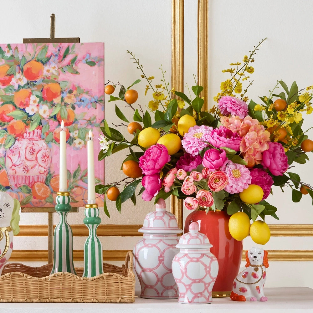 A colorful vignette with pink-patterned ginger jars, vibrant flowers, citrus fruits, and green striped candlesticks.