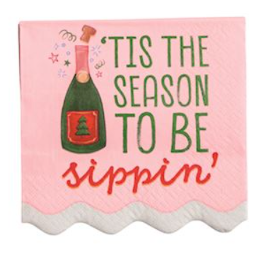 Pink napkin reading "'Tis the season to be sippin'" next to a popping champagne bottle.