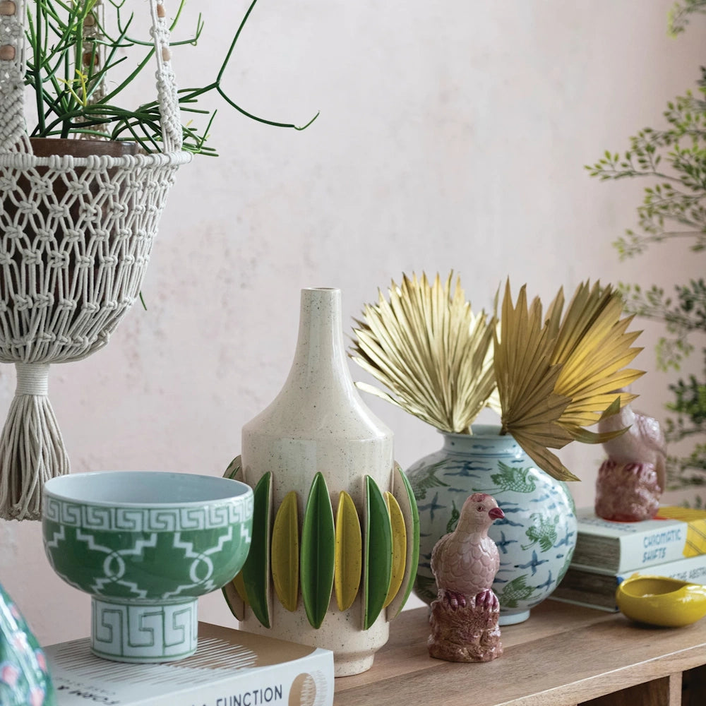 Hand-painted pink stoneware bird figurine on a wooden shelf with ceramic vases and a macrame hanging planter.