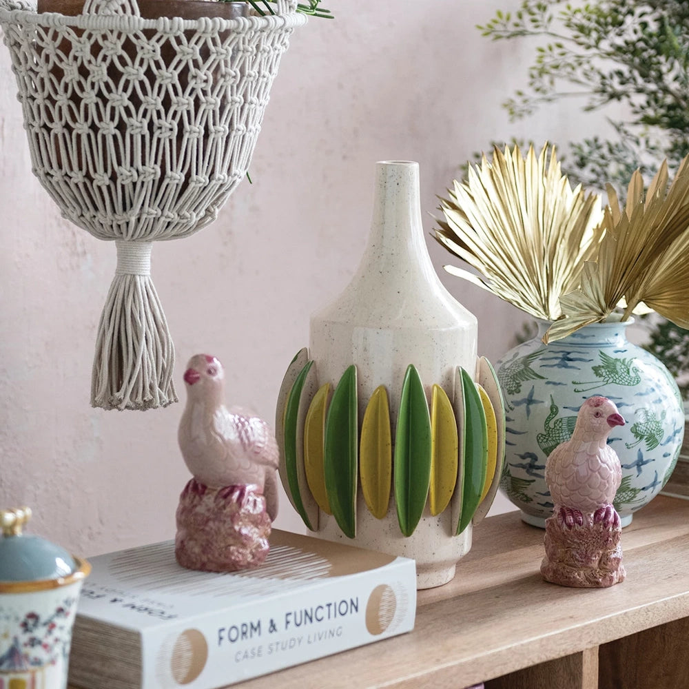 Pink hand-painted stoneware bird figurines styled on a wooden shelf with a macramé planter and modern ceramic vases.