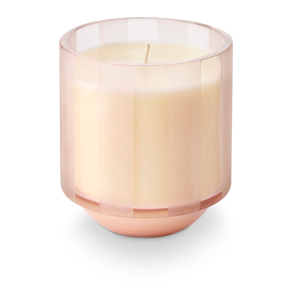 An unlit candle in a translucent pink etched-stripe glass jar.