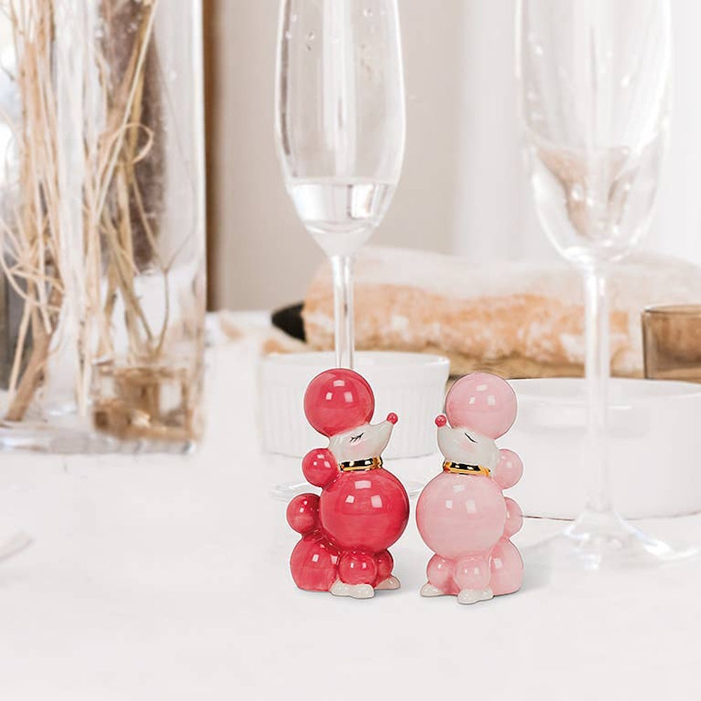 Pink and red ceramic poodle salt and pepper shakers on a white dining table with champagne glasses.