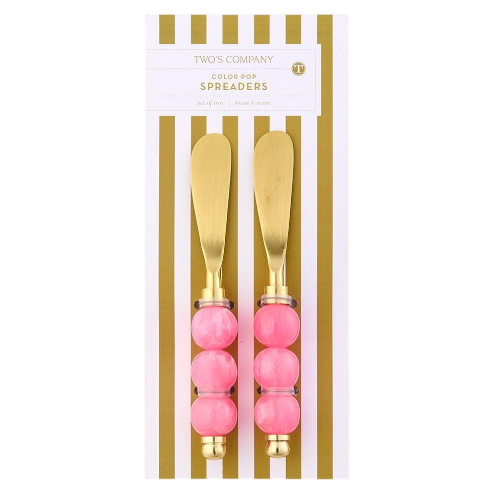 Set of two gold spreaders with pink beaded handles presented on gold-striped card packaging.