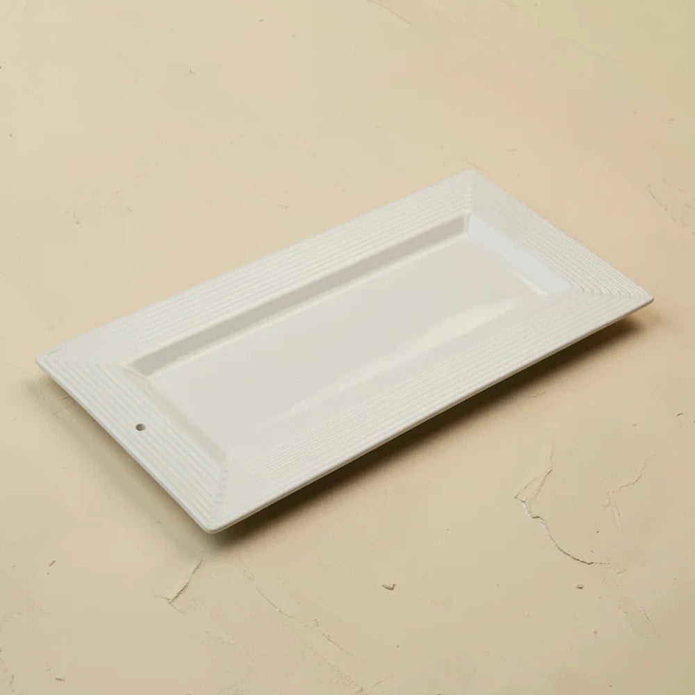 A rectangular white ceramic serving tray with ridged borders and a small hole on one side.