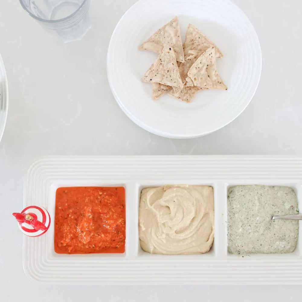 A 3-section white ceramic serving dish with red, tan, and green dips, featuring a striped holiday charm.