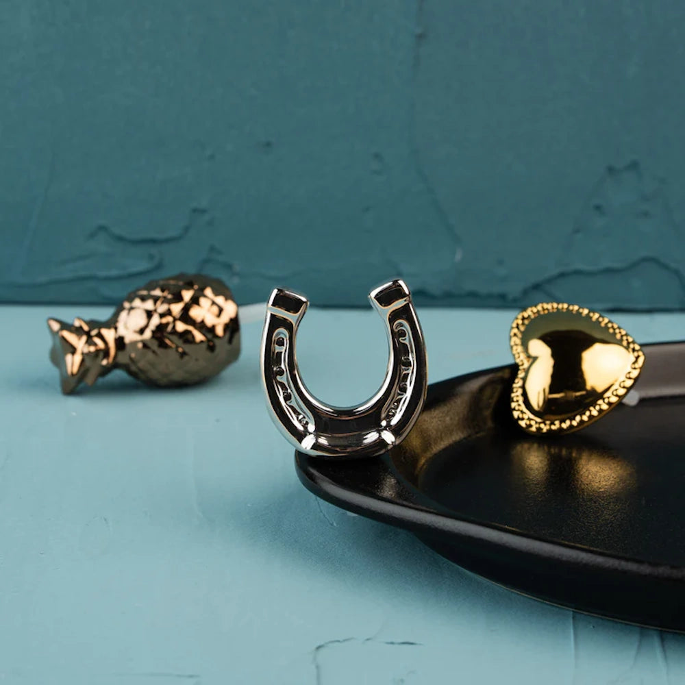 A silver horseshoe charm on a black tray alongside a gold heart charm against a teal textured background.