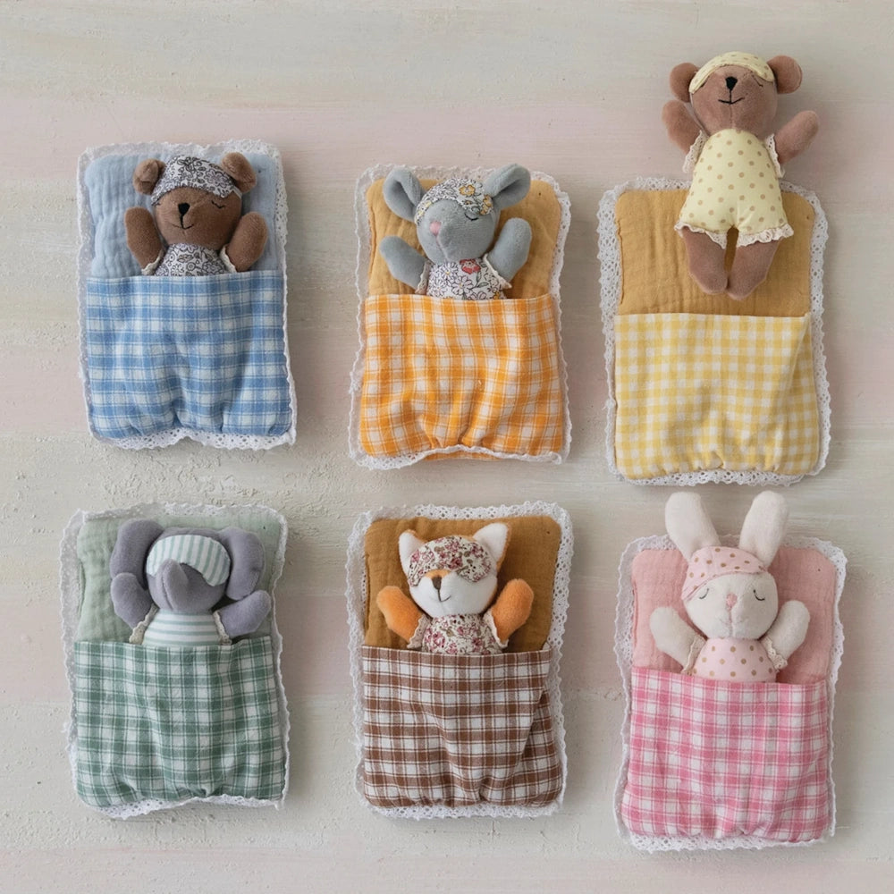 Six plush animals in sleeping bags arranged on a light surface, with one plush bear resting outside its bag.