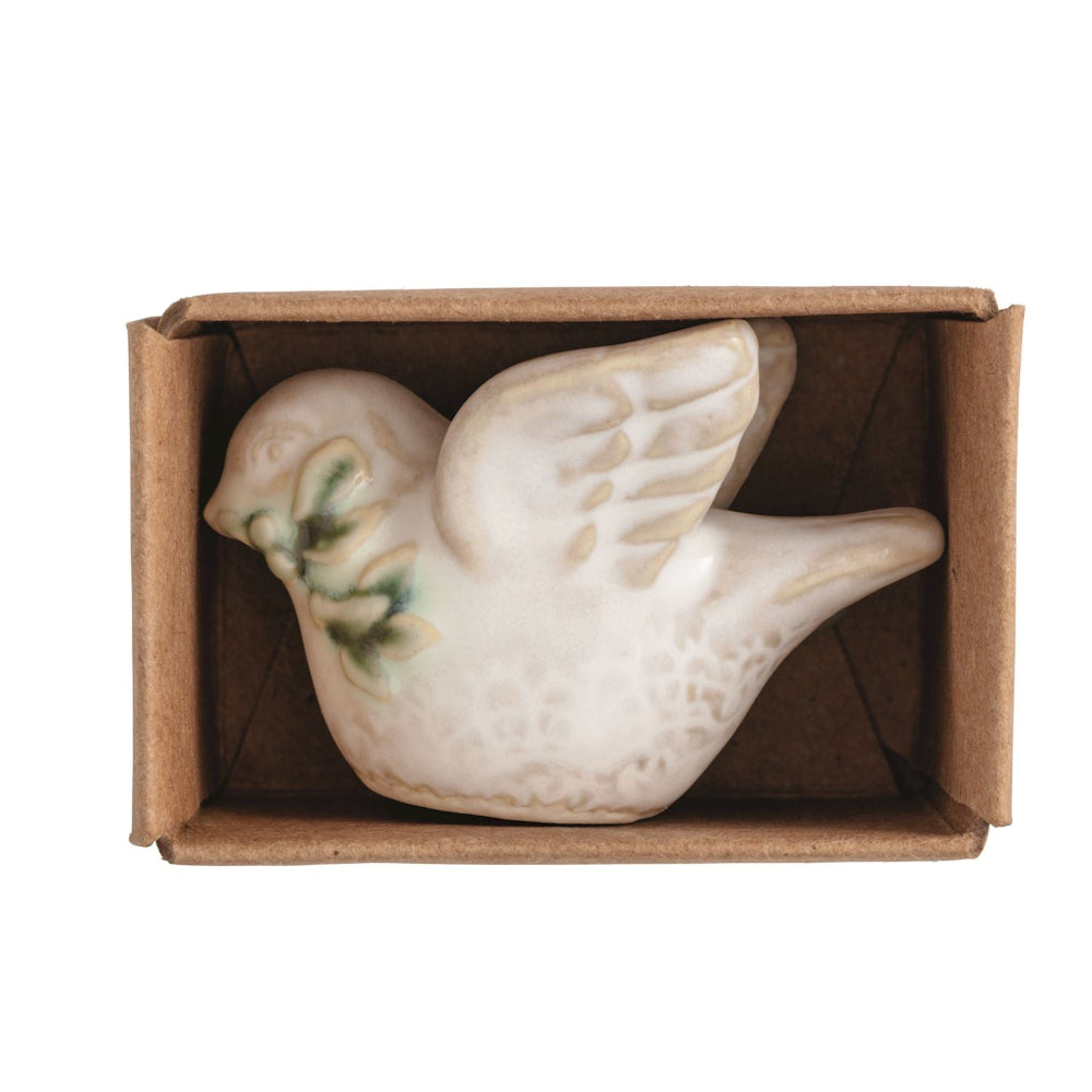 Miniature white ceramic dove figurine resting inside a small brown cardboard box.