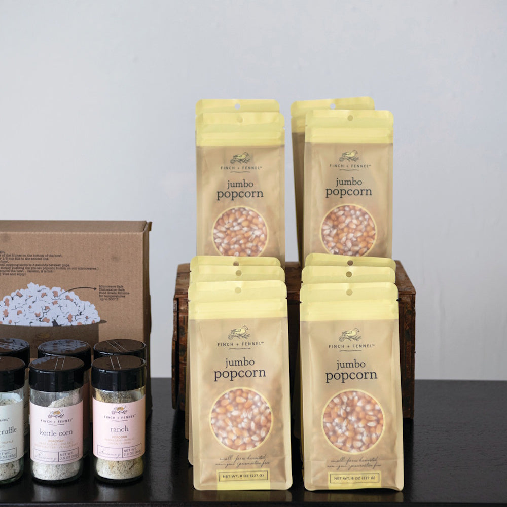 Several stand-up pouches of Finch + Fennel jumbo popcorn kernels displayed next to seasoning jars.