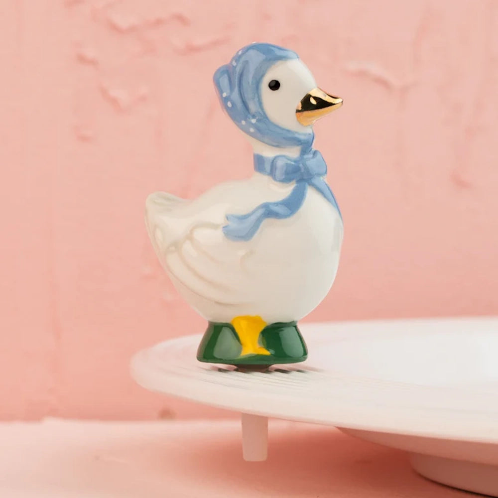 Small ceramic goose figurine wearing a blue bonnet with a tied bow and a gold beak.