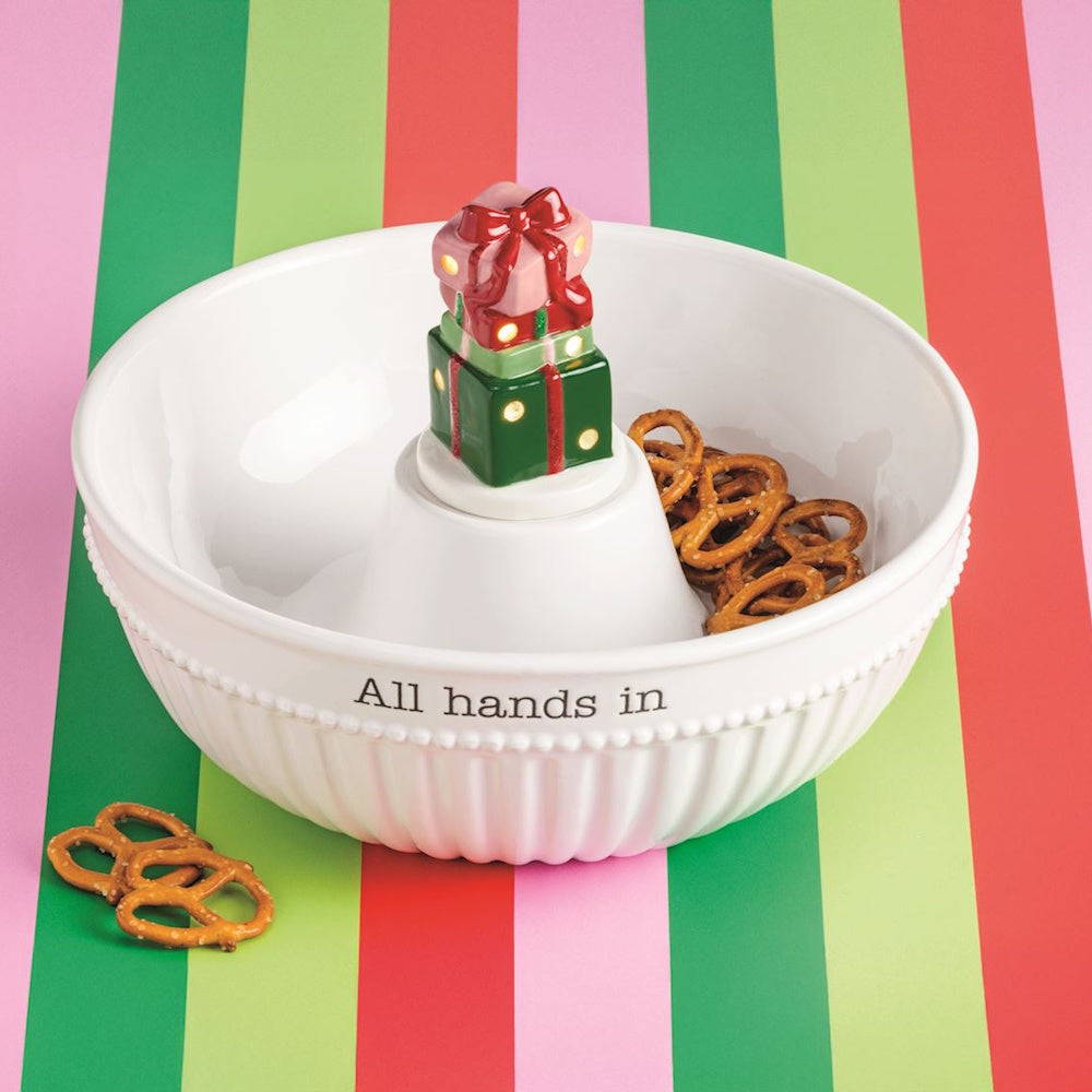 White serving bowl with stacked light-up present gifts centerpiece, labeled "All hands in."
