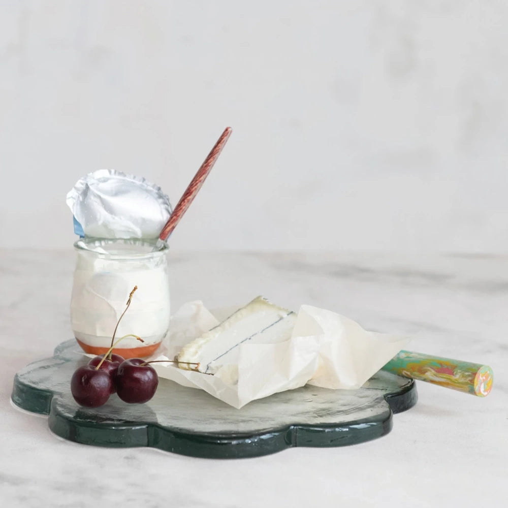 Scalloped green pressed glass cheese board with a wedge of brie, fresh cherries, and a small yogurt jar.