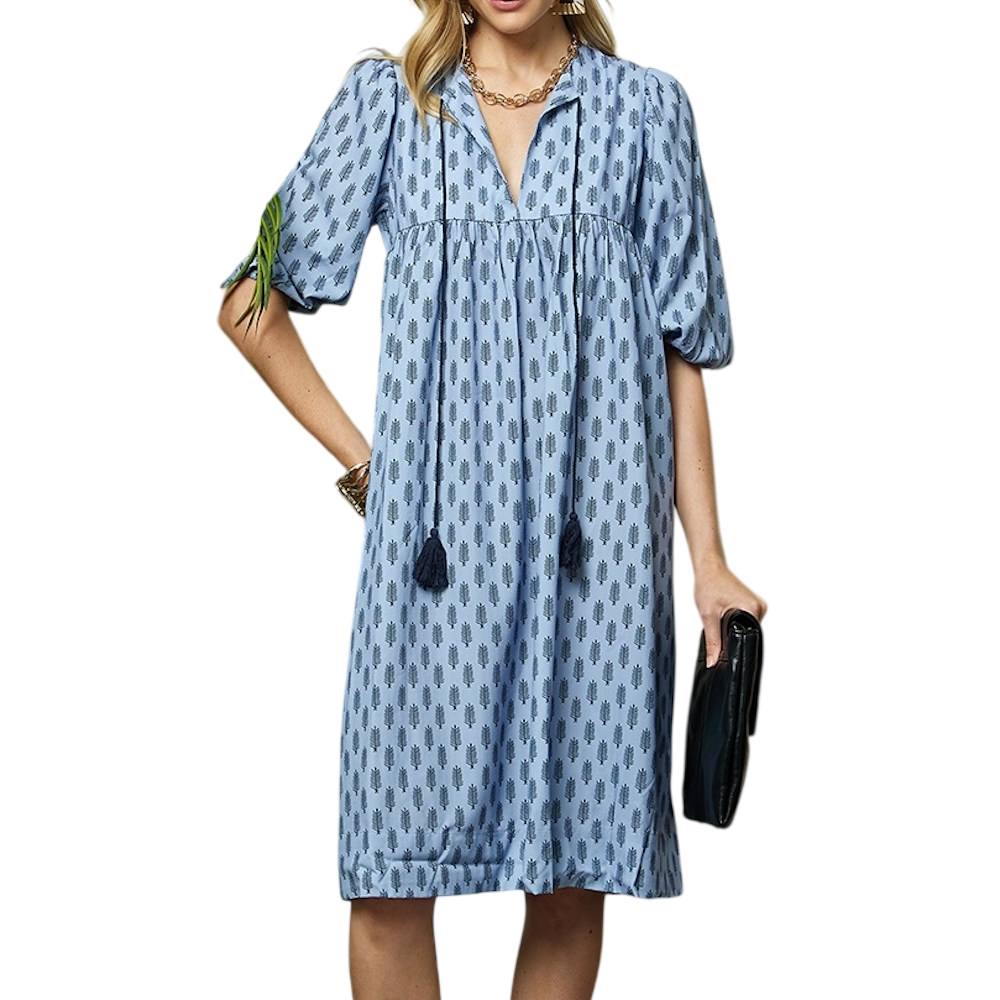 Woman wearing a light blue midi dress with a dark blue tree pattern, puff sleeves, and tassel ties.