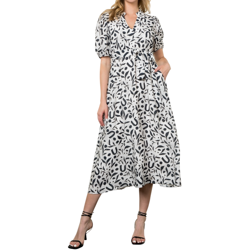 Woman wearing a black and white patterned maxi dress with puffed sleeves, a waist tie, and black heels.