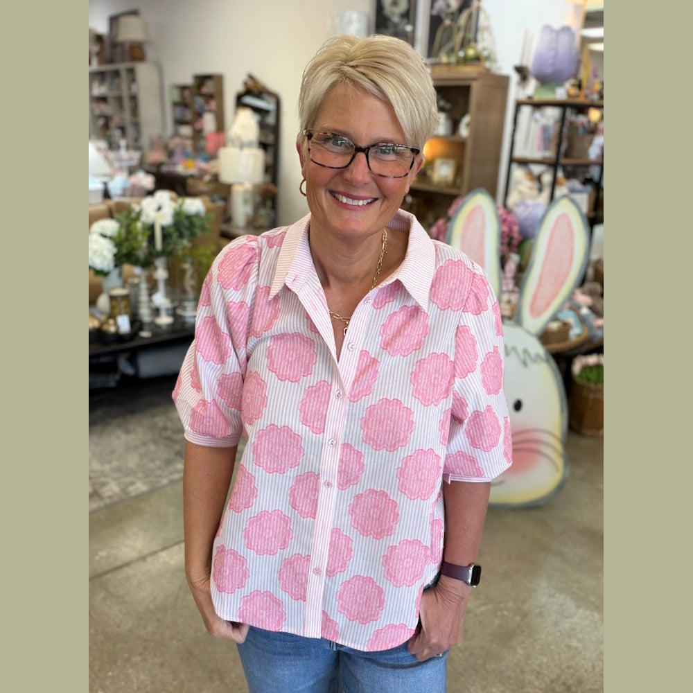 Woman in a pink and white striped puff-sleeve shirt with large floral patterns, smiling in a boutique setting.
