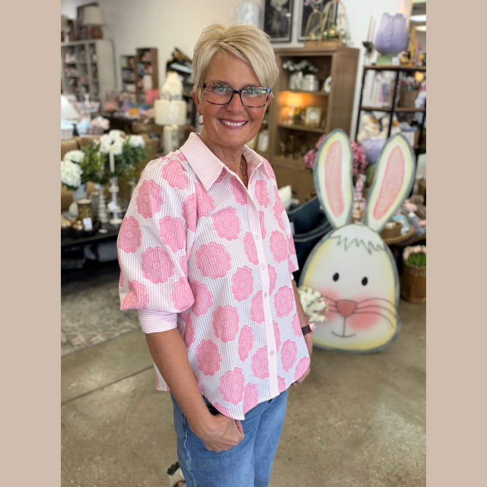 Woman wearing a pink and white striped shirt with puff sleeves and floral print.
