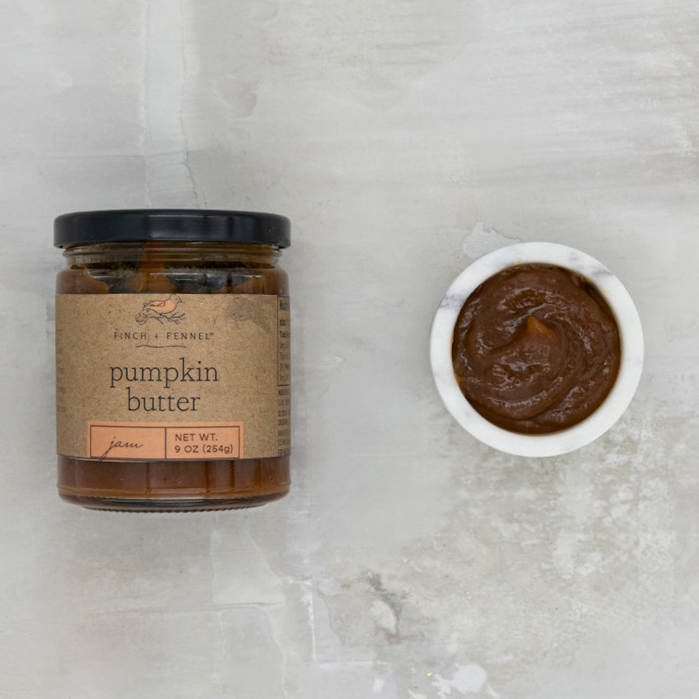 A jar of Finch + Fennel pumpkin butter next to a small white bowl of the spread on a grey surface.