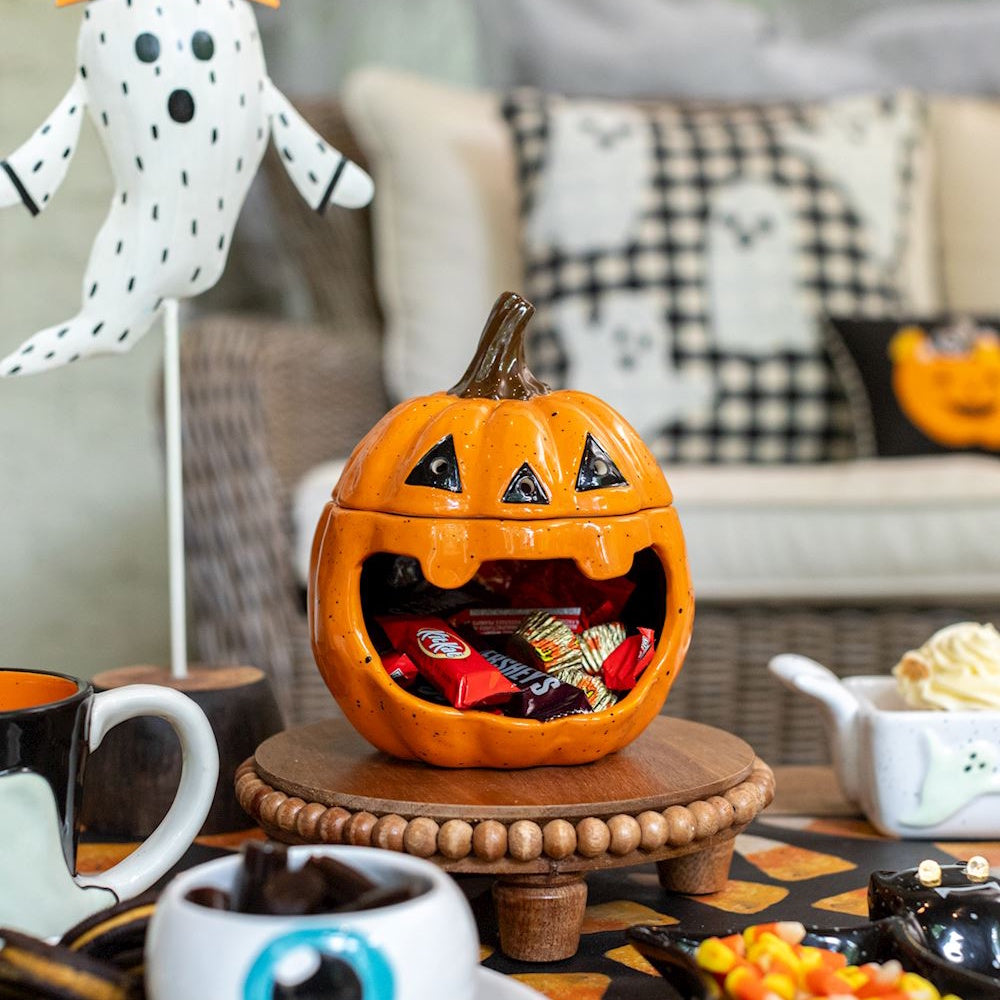 Ceramic pumpkin candy bowl filled with Halloween chocolates on a festive table display.