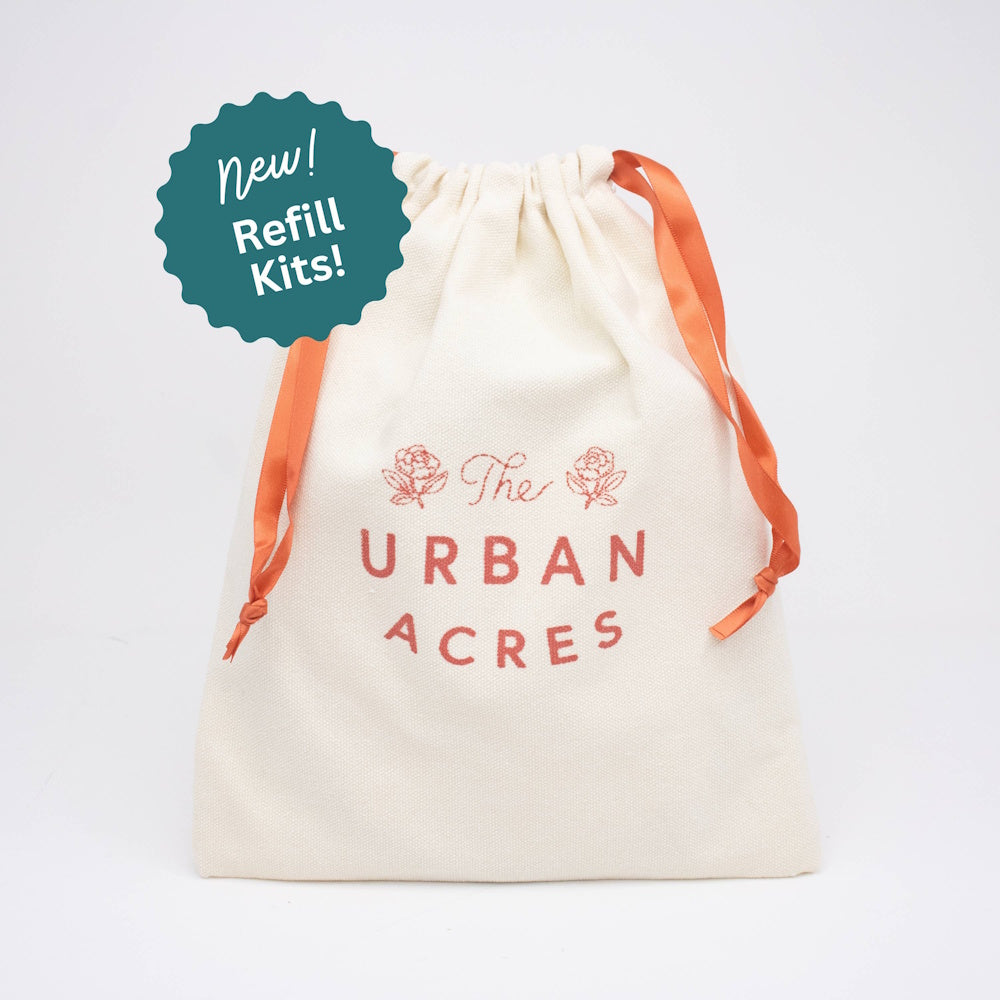 Cream canvas drawstring bag printed with "The Urban Acres" and orange ribbon ties.