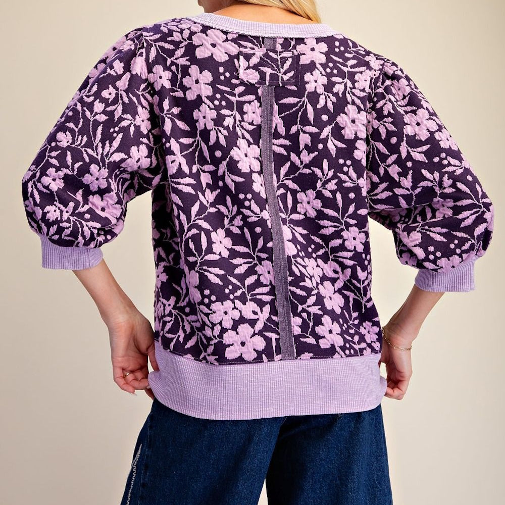 Back view of a purple floral textured sweatshirt with puffed 3/4 sleeves and ribbed hem.