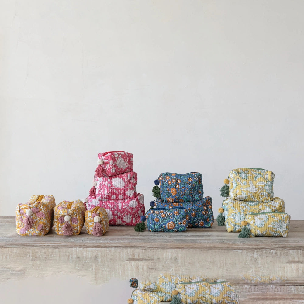 Quilted cotton floral zip pouches in pink, blue, yellow, and orange with decorative tassels on a rustic wood surface.