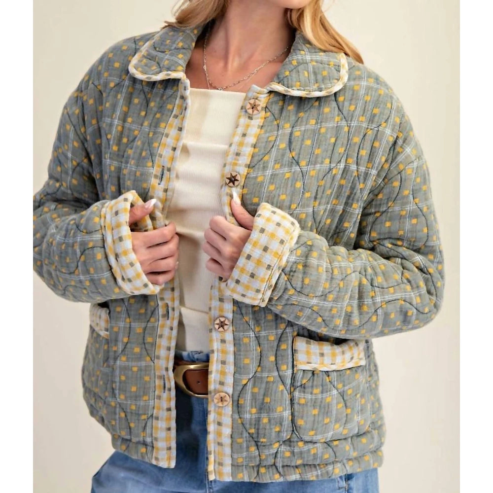 Front view of a green mineral-washed quilted jacket with star buttons and plaid cuffs being held open.