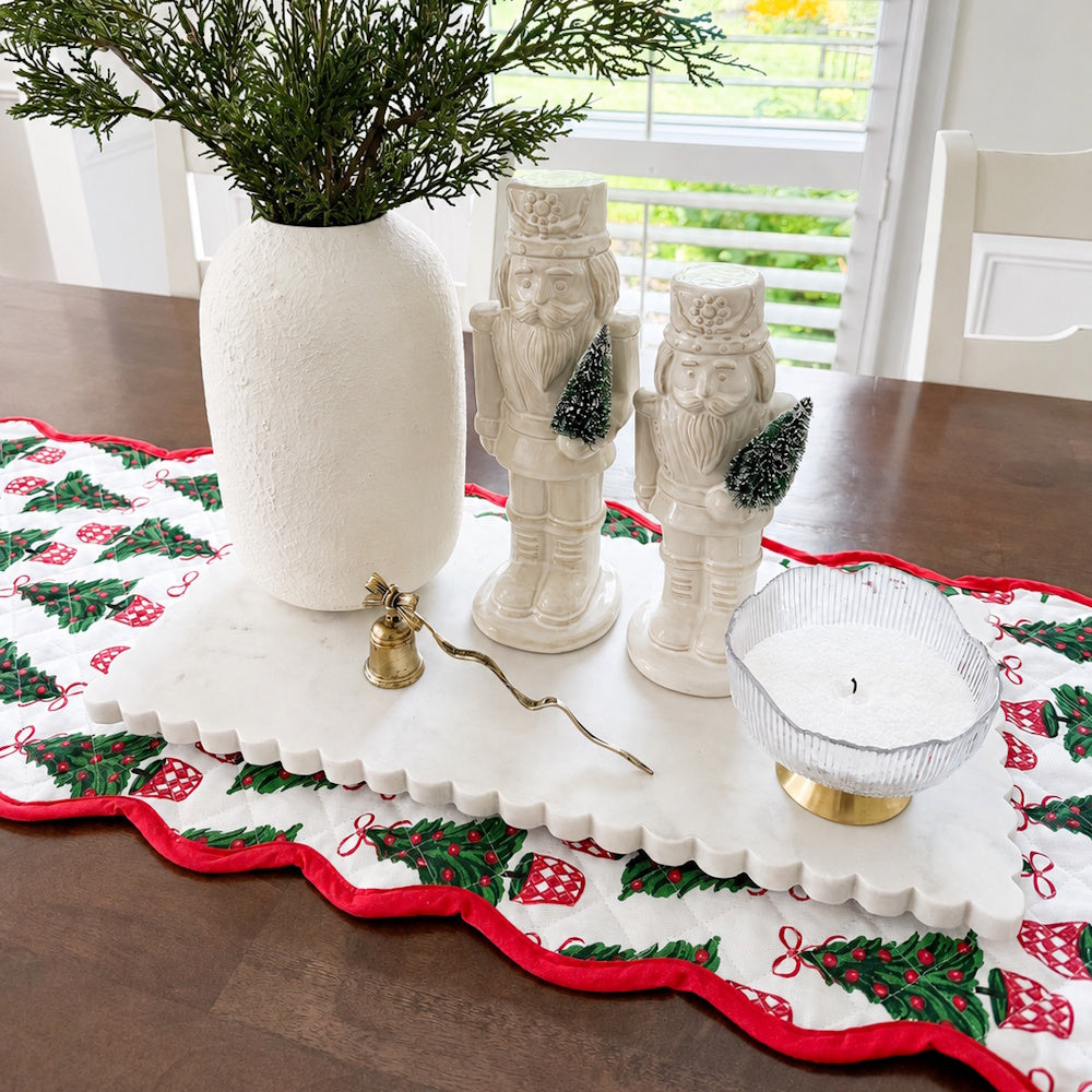 Quilted Christmas table runner displaying nutcrackers, a vase, a candle, and a bell on a tray.