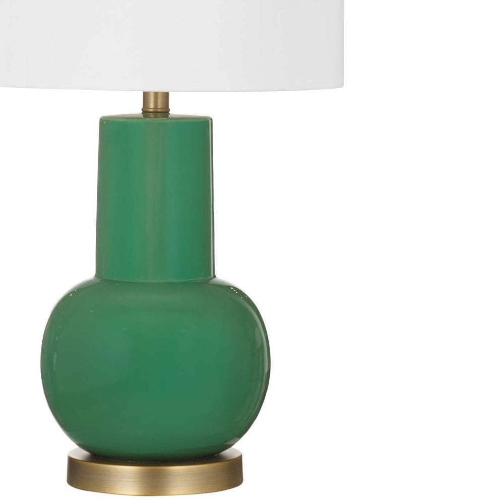 Close-up of a glossy green ceramic lamp base with brass accents and a white fabric shade.